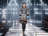 A fashionable model is walking on the T-stage wearing modern clothing integrated with ethnic minority elements. The lights are shining.