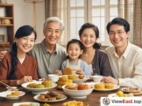 A family is sitting around a table, with smiles on their faces. There are delicious foods and mooncakes on the table.