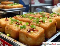 On a Hunan snack street, a shop displays freshly fried stinky tofu, crispy on the outside and soft on the inside, with the aroma of chili and scallions making mouths water.