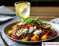 A quinoa salad with roasted vegetables and goat cheese in a modern minimalist restaurant, next to a glass of iced lemon water.