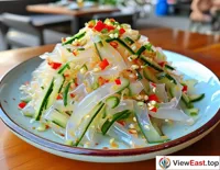 A plate of jellyfish salad with cucumber and red pepper shreds at a seaside restaurant, perfect for a summer day.
